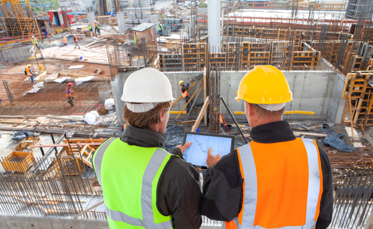 A construction worker discussing construction plans with an architect who is holding a tablet.