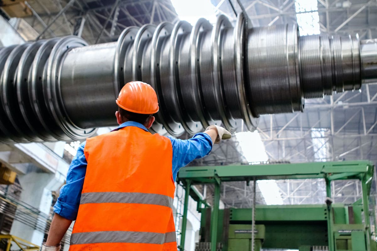 A man in an orange hard hat and vest is checking a factory machine.